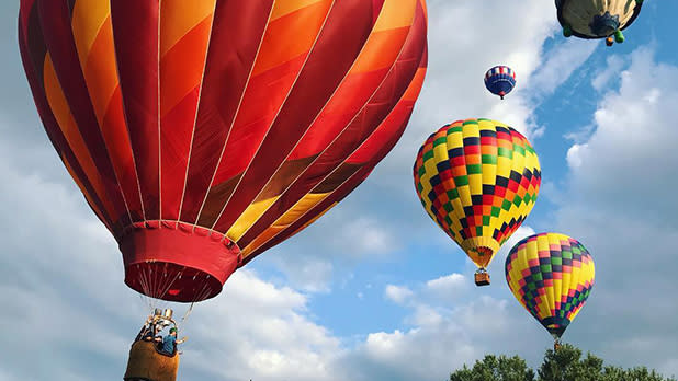 Multicolored hot air balloons flying above head at Spiedie Fest in Binghamton on a partly cloudy summer day