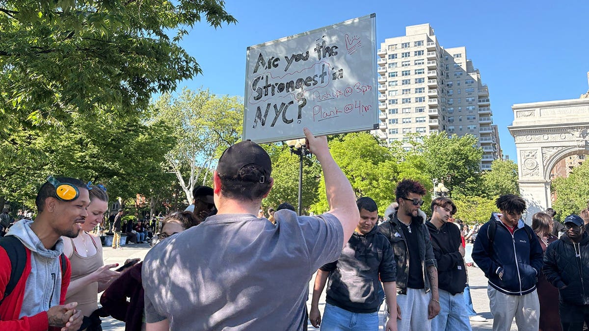man holds "Are you the strongest in NYC?" sign