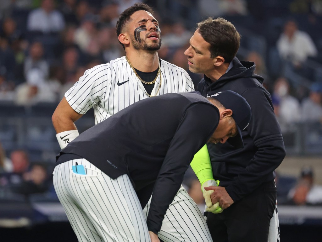 New York Yankees shortstop José Caballero reacts in pain after being hit by a pitch, as manager Aaron Boone and a trainer check on him.