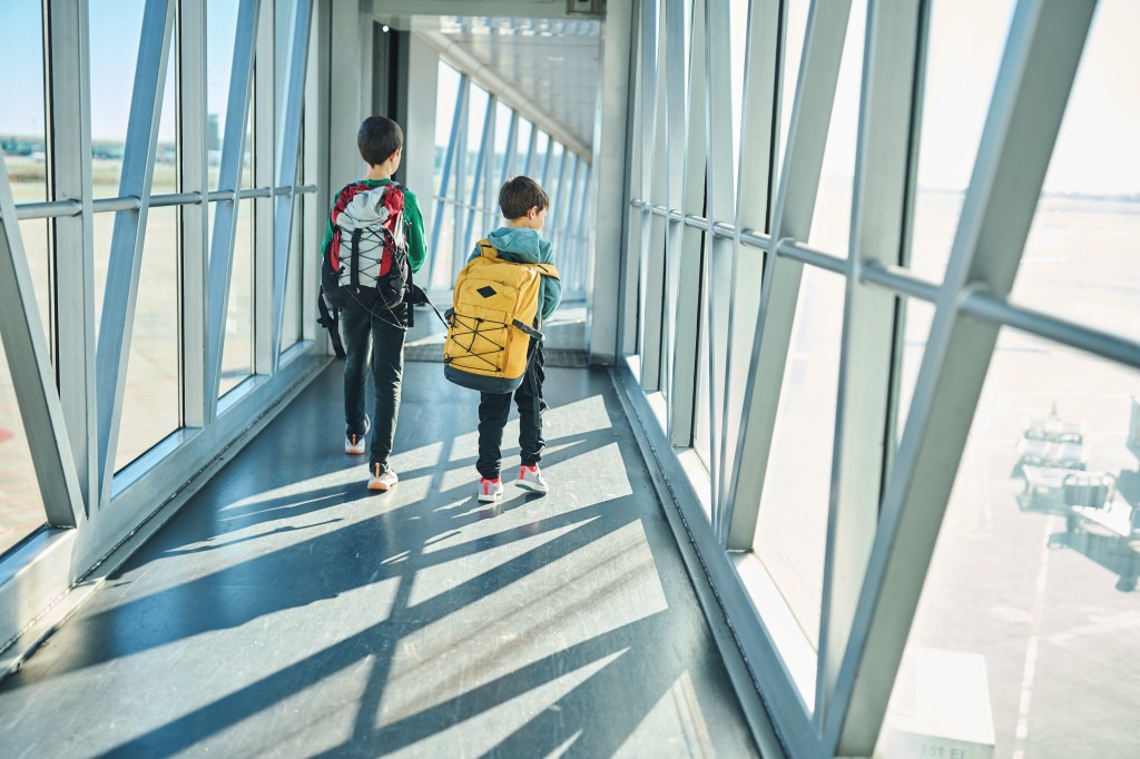 Two kids with backpacks walking through an airport jet bridge.