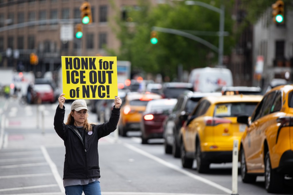 A woman holds a yellow sign that reads "Honk for ICE Out of NYC!" at an immigration protest in New York City.