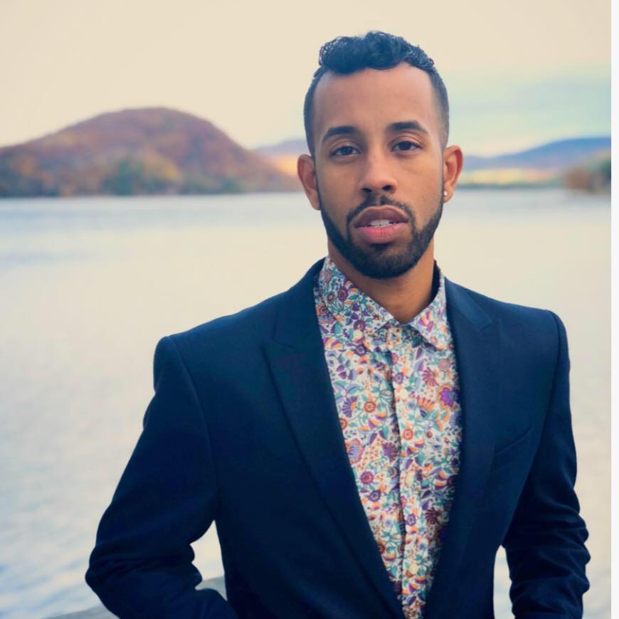 Michael-Anthony Souza standing by a lake with a hill in the background.