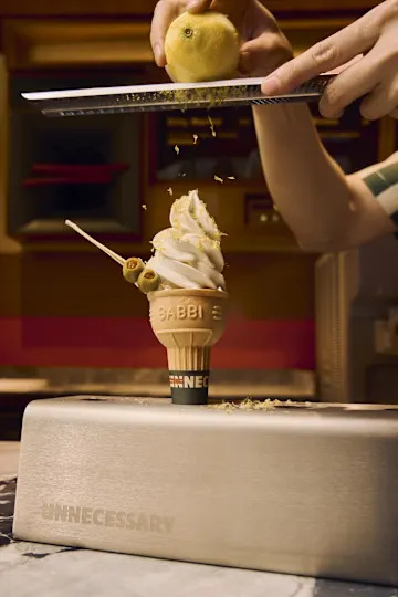 Someone zesting a lemon onto an ice cream cone with olives on it.