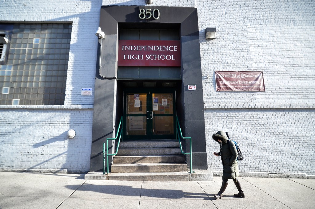 A student walks past the entrance of Independence High School, which has a sign for "ACADEMIC EXCELLENCE AND RESTORATIVE PRACTICES".