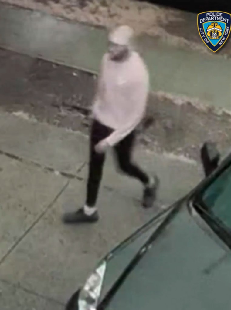 Surveillance footage of an individual in a light-colored sweatshirt and dark pants walking on a sidewalk next to a car.