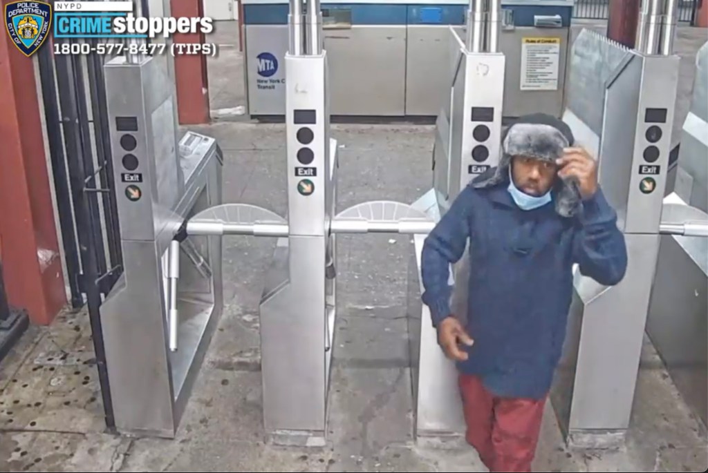 Surveillance photo of a man in a blue sweater, red pants, a winter hat, and a blue face mask around his chin, exiting a subway station through a turnstile.