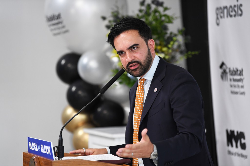 NYC Mayor Zohran Mamdani speaking at a podium with "BLOCK by BLOCK" and "Habitat for Humanity" logos visible in the background.