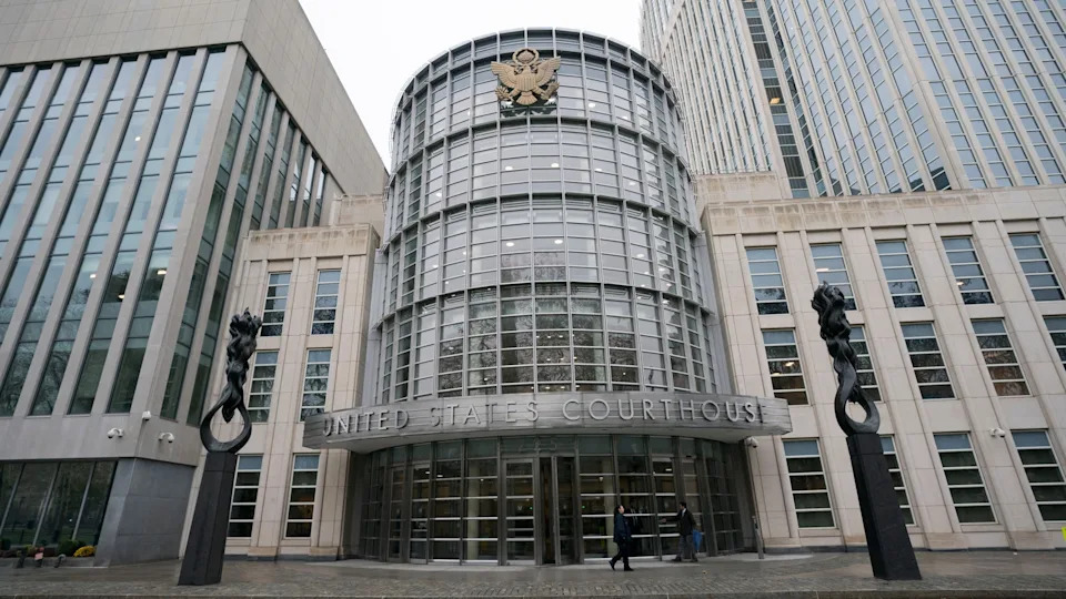 The image shows the exterior of a United States Courthouse with a modern glass facade and the emblem above the entrance.