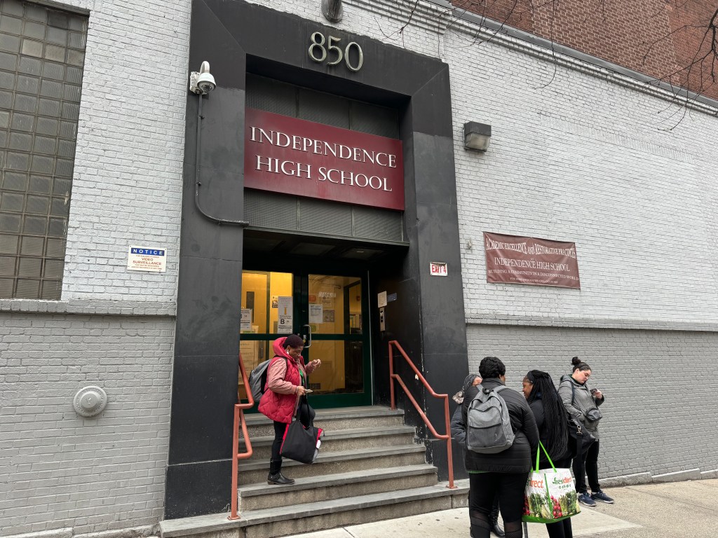 Students stand on the steps and sidewalk outside Independence High School, where a video surveillance notice is posted on the wall.