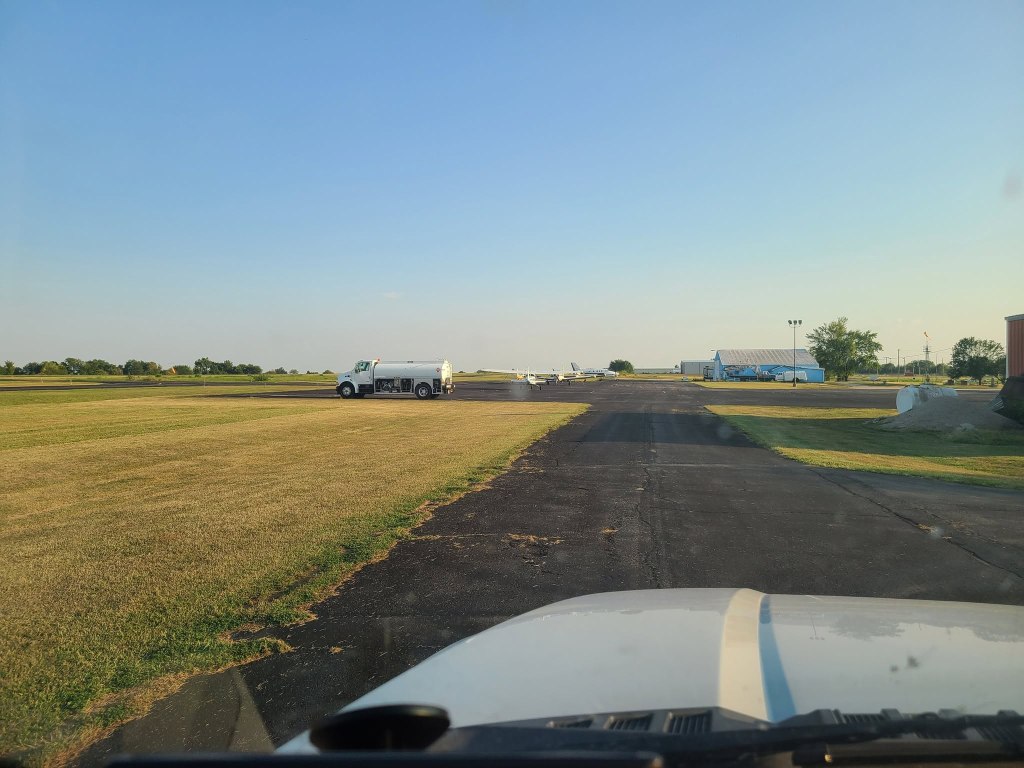 An airport runway with a fuel truck and small planes on the tarmac.