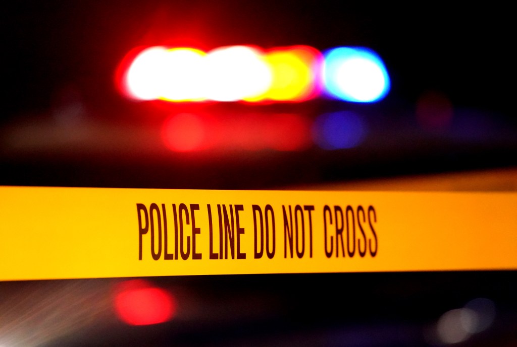 Yellow police tape with "POLICE LINE DO NOT CROSS" written in black, with blurred red and blue lights in the background.