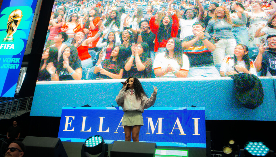 A performer on stage faces a cheering crowd shown on a large screen at a FIFA World Cup event.
