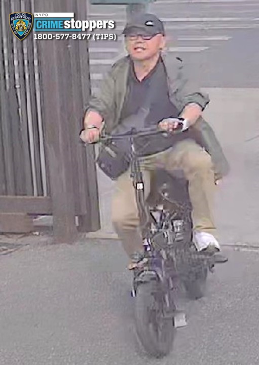 Surveillance footage of an Asian man wearing a green jacket, tan pants, black shirt, black baseball cap, and glasses, riding a black bicycle.