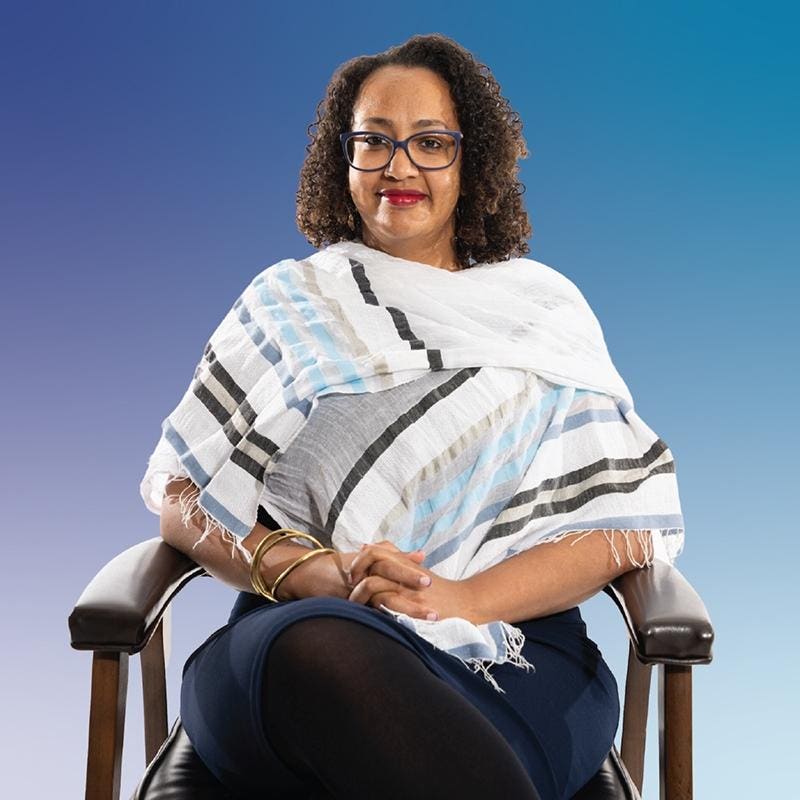 Photo of a Black woman with curly hair and red lipstick and glasses smiling.