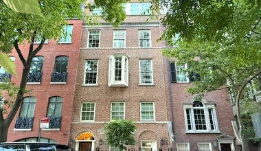 Facade of a brick building with a mix of large windows, greenery in the foreground, and a decorative entryway.