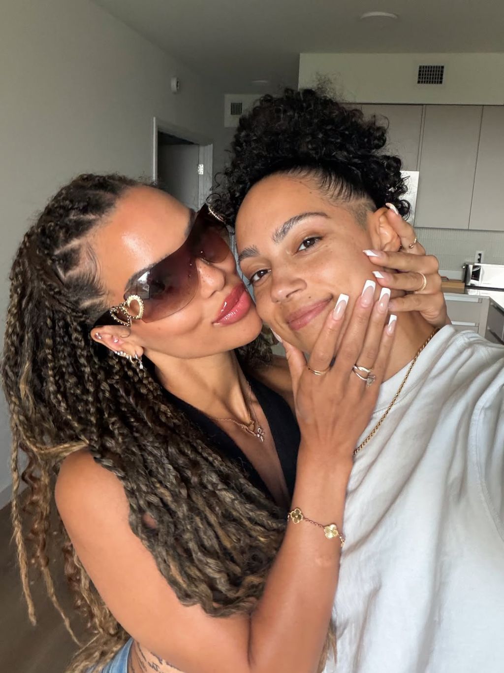 Two women with curly hair embracing and smiling affectionately.