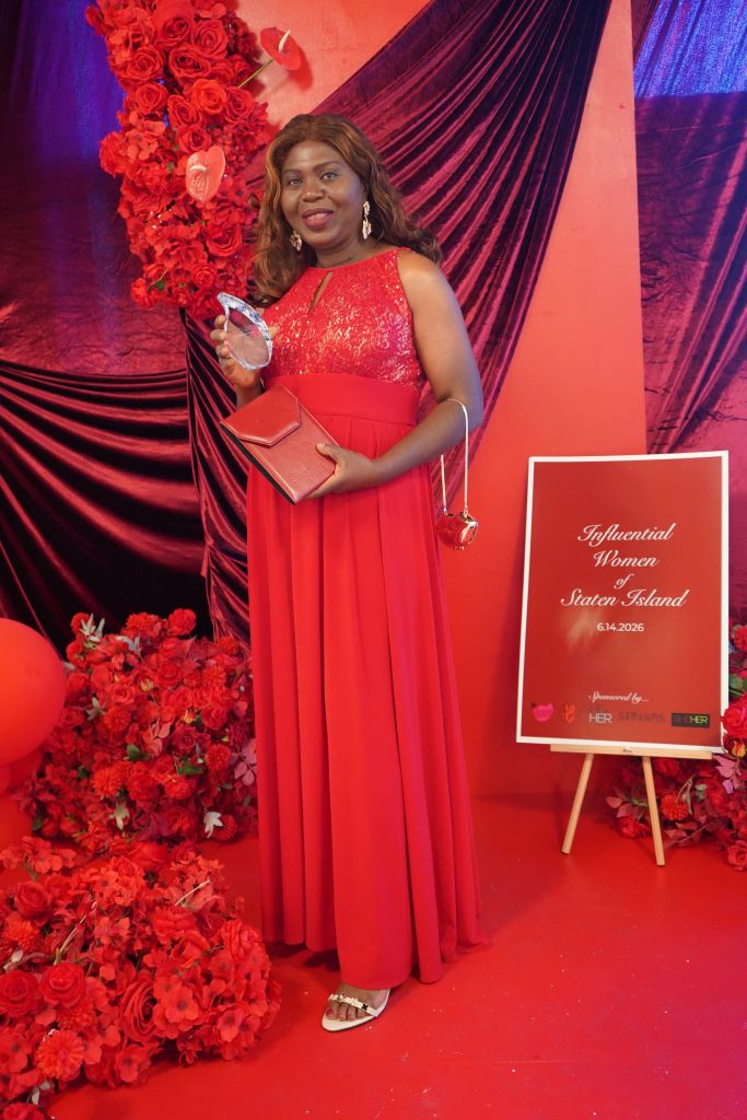 A woman in a red sequin dress holding an award stands in front of a backdrop of red flowers and purple curtains. The sign behind her reads "Influential Women Staten Island 6.14.2026".