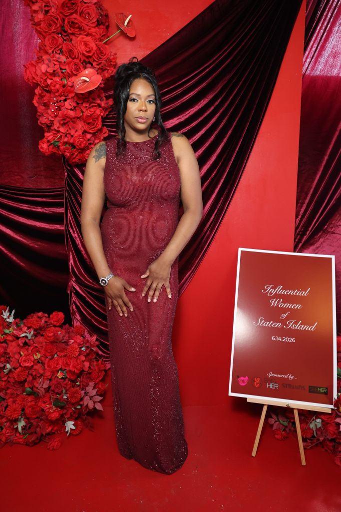 A woman in a red sequin dress stands in front of a red floral backdrop, holding a sign that says "Influential Women of Staten Island 6.14.2026".