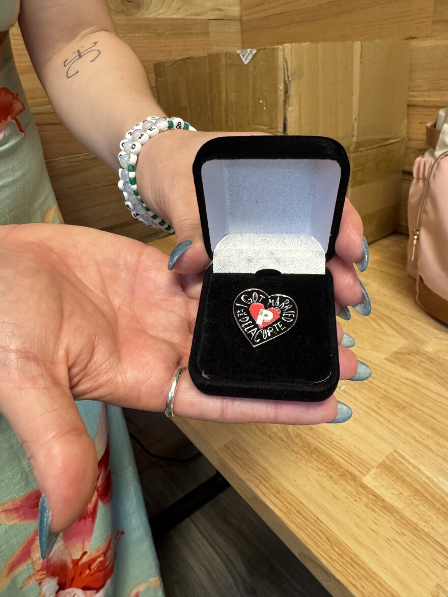 Wedding planner Carla Perez holds up a special pin that the Public had made for each of the couples getting married at the Delacorte.