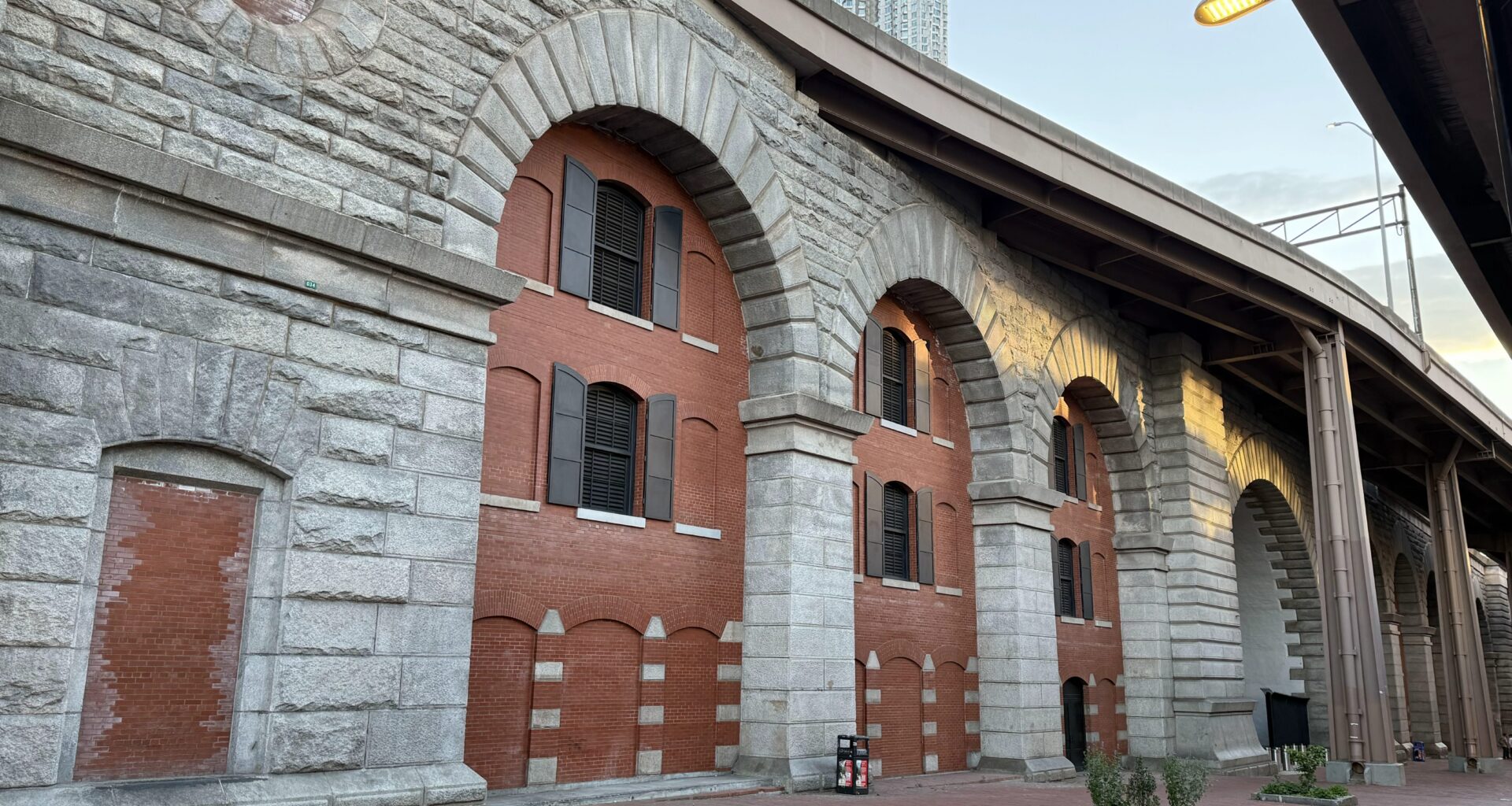 Historical brick and stone archway structure with windows, situated alongside a paved walkway.
