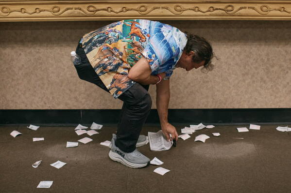 A man picks up his glasses and track program next to discarded betting slips on closing day at Aqueduct Racetrack in the Queens borough of New York, Sunday, June 28, 2026. (AP Photo/Andres Kudacki)