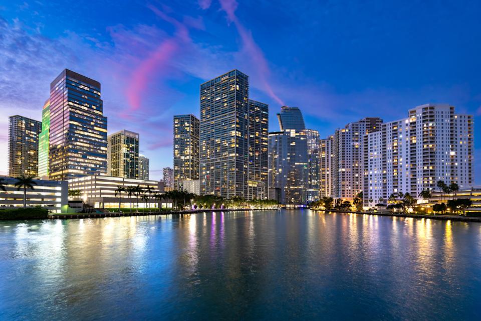 The skyline of the Brickell neighborhood in Miami, with illuminated buildings and palm trees under a colorful twilight sky.