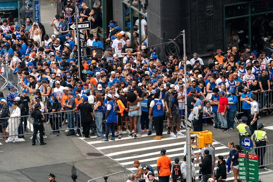 A large crowd wearing sports jerseys and apparel gathers on a city street, with police officers managing the scene from nearby