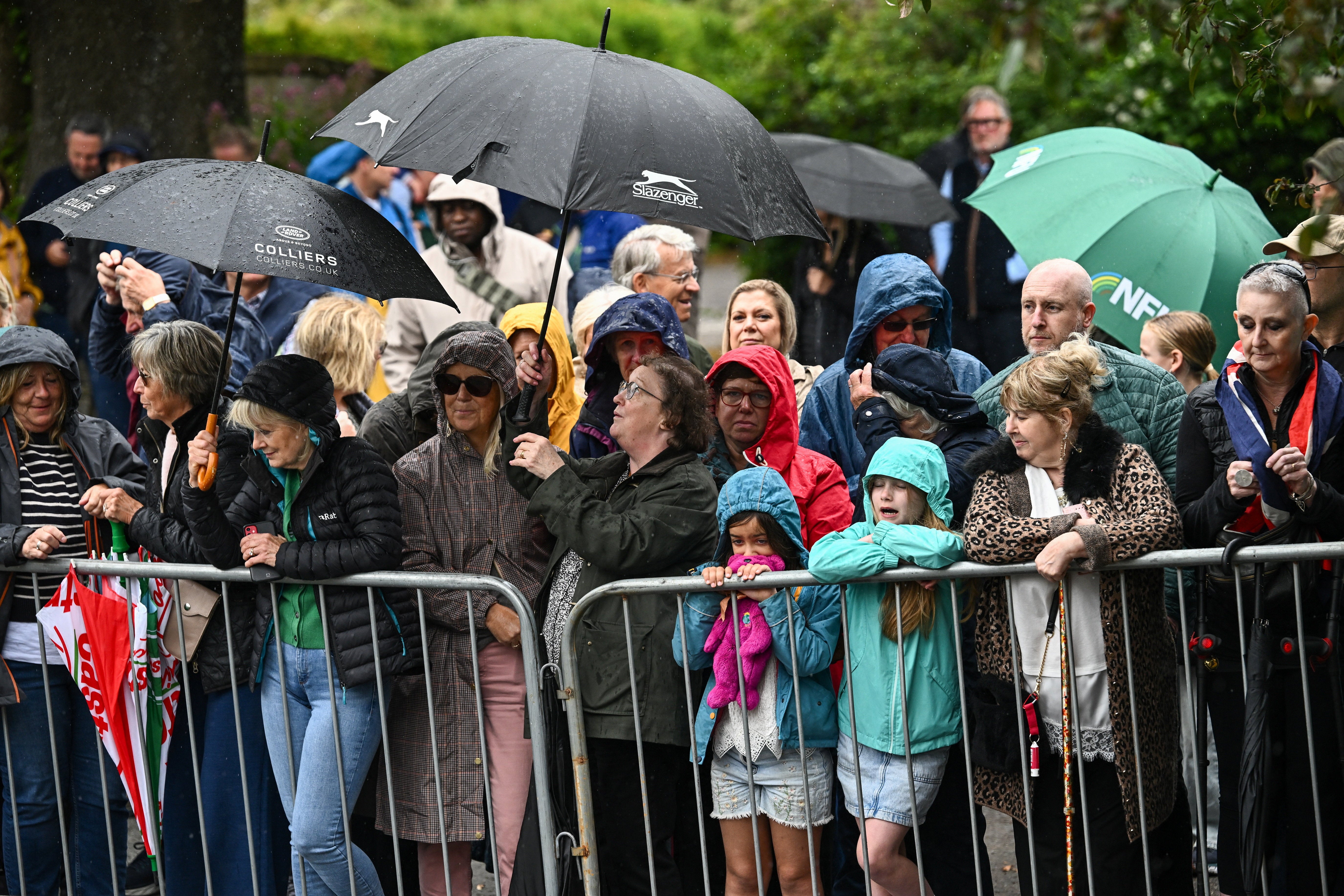People use umbrellas to shield from the rain as they gather outside All Saints' Church