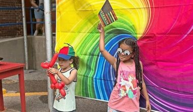 Kids posed in front of the rainbow swirl tapestry, one showing off a new balloon-animal dog, and another holding a mini Juneteenth flag high.
