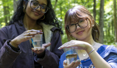Two students pose together holding trout fingerlings in a cup, poised to be released into a stream