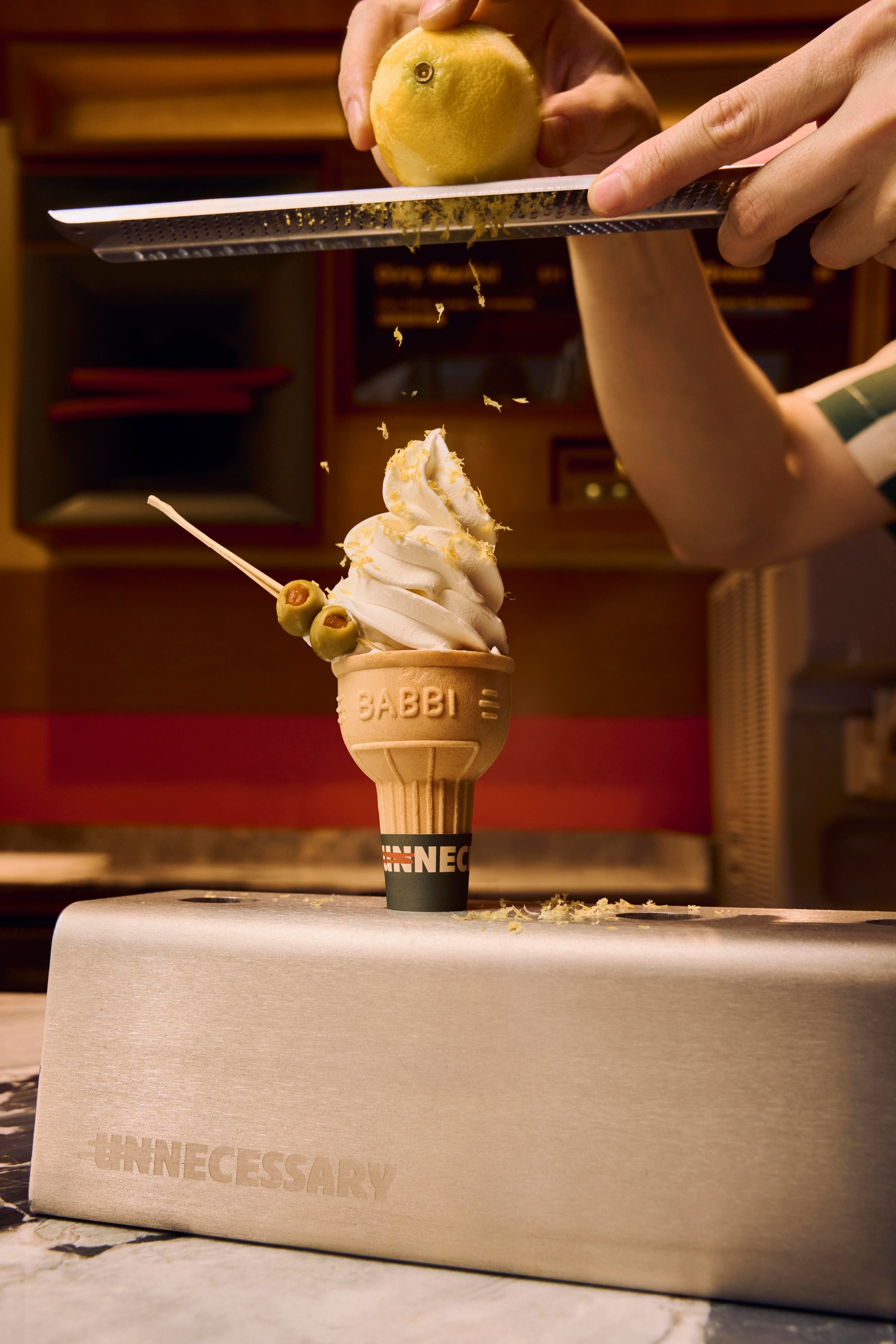 Someone zesting a lemon onto an ice cream cone with olives on it.