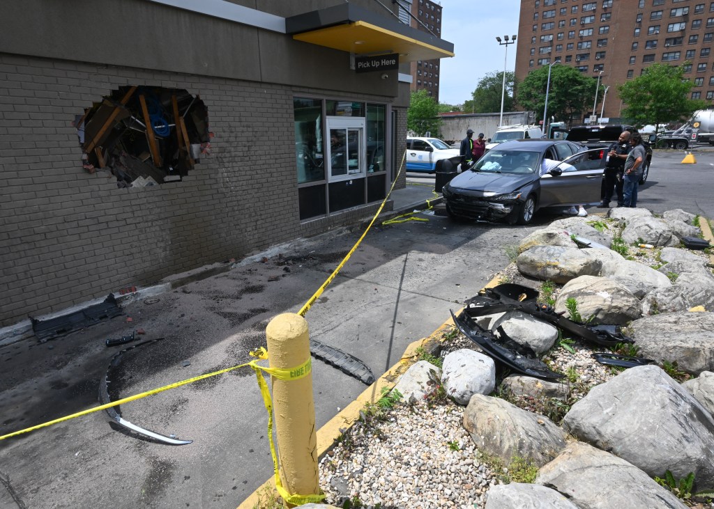 A car crashed into the side of a McDonald's building, leaving a large hole in the brick wall and debris scattered on the ground, with a yellow police tape sectioning off the area.