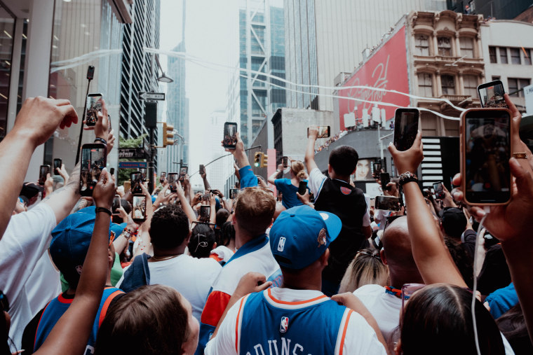 People hold their phones up to improve their views of the parade floats on Maiden Lane and Broadway.