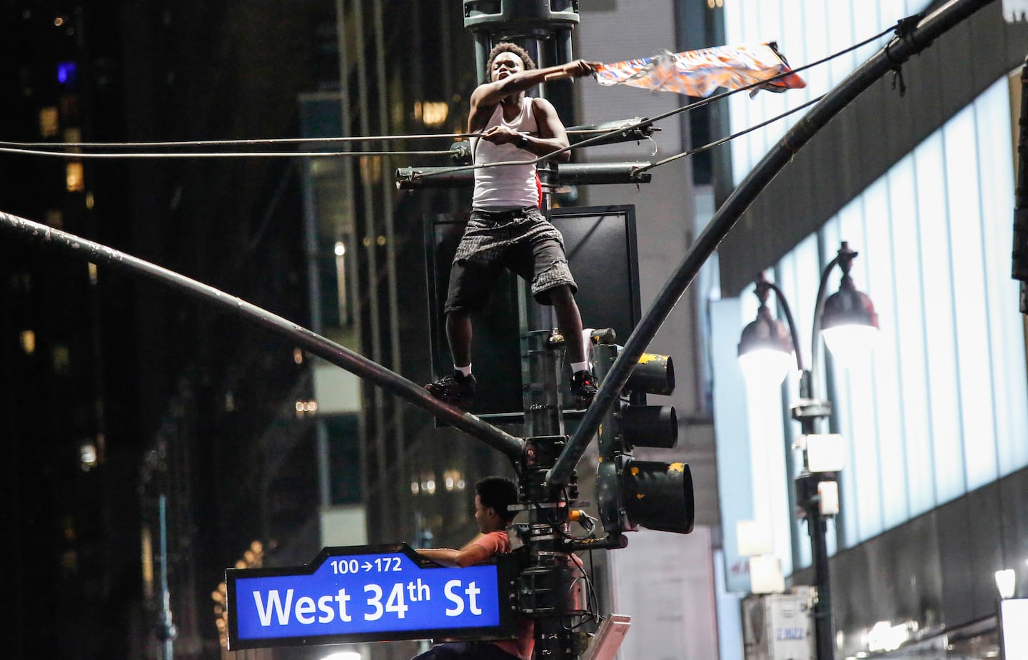 A Knicks fan waves a flag while standing on top of a traffic light poles after the New York Knicks defeated the San Antonio Spurs in Game 5 of the NBA Finals to win the series, in New York, on June 14, 2026. The Knicks won the NBA Championship for the first time since 1973, for the third time in franchise history.