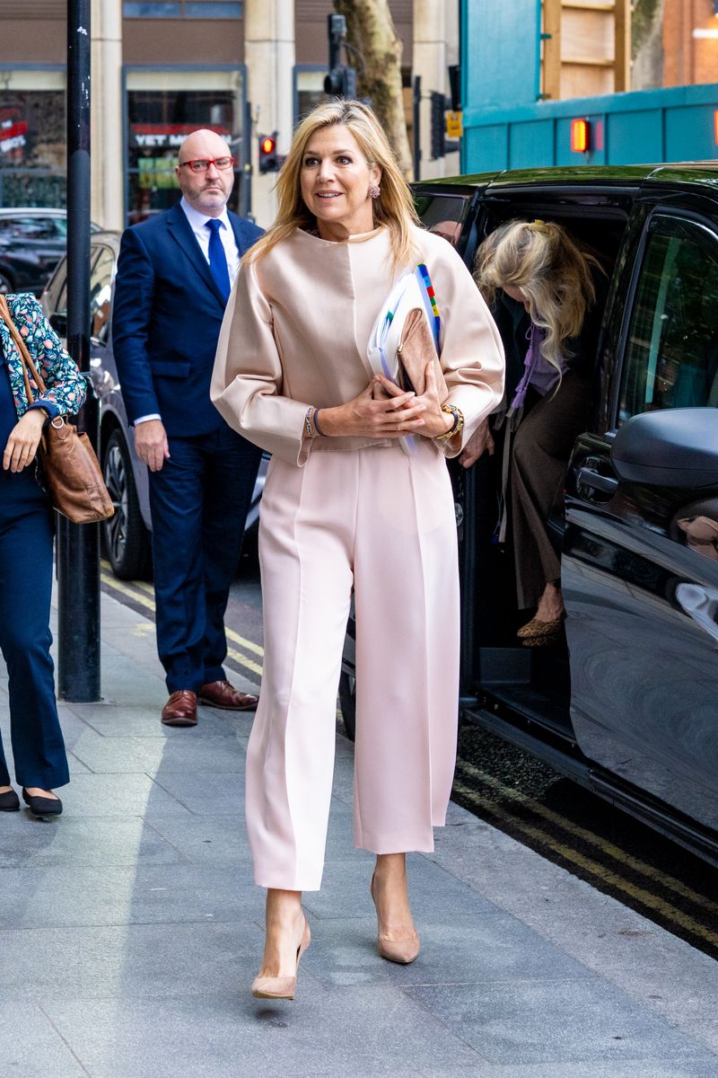 Queen Máxima arrived in London wearing a structured satin jacket paired with flowing wide-leg trousers in coordinating soft pink hues.