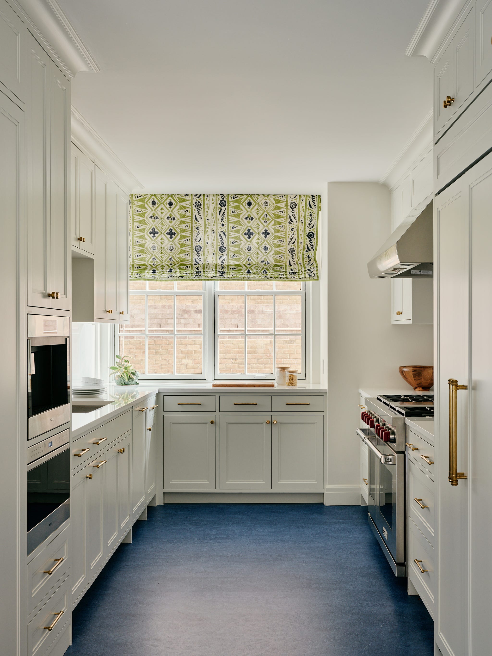 Modern kitchen with white cabinets, blue floor, and patterned green window shade.