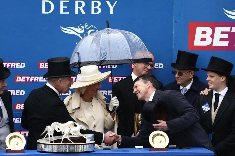King Charles shaking hands with a horse trainer while standing with Queen Camilla