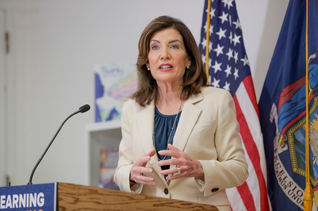 Kathy Hochul speaking at a podium with US and New York state flags behind her.