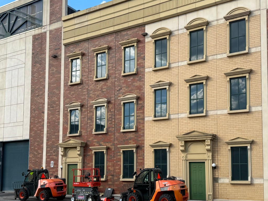 Facade of a two-tone brick building with large windows, featuring a mix of red and tan brickwork, accompanied by construction equipment in the foreground.