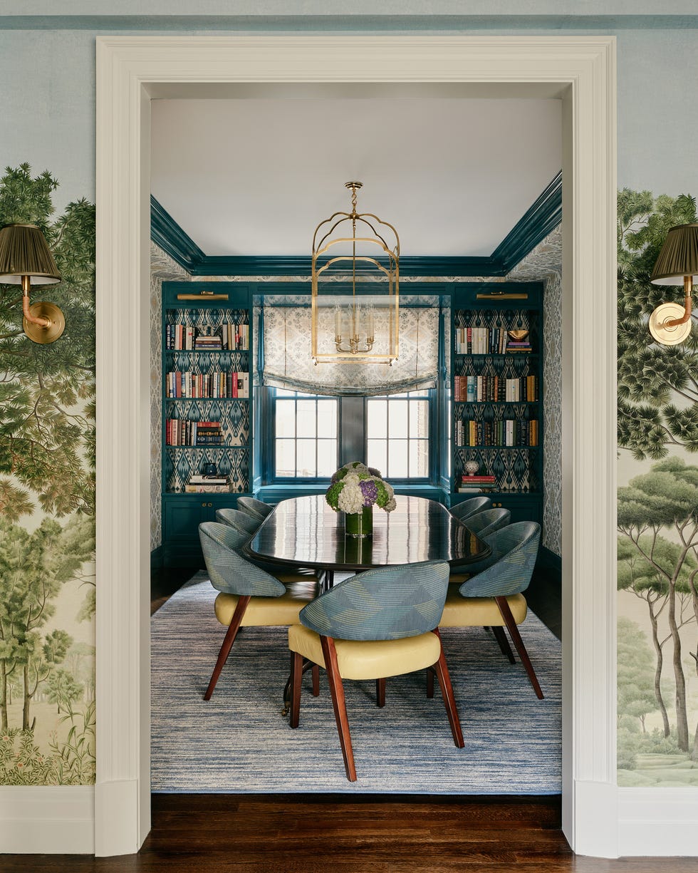 Elegant dining room with a long table, surrounded by bookshelves, and walls featuring tree murals.