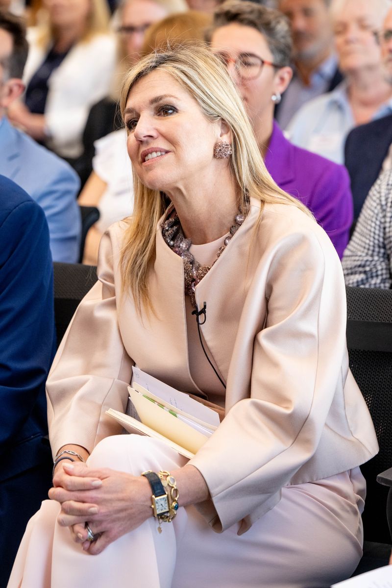 Queen Máxima accessorized her monochromatic look with a gemstone necklace, coordinating earrings, and a blush suede clutch.
