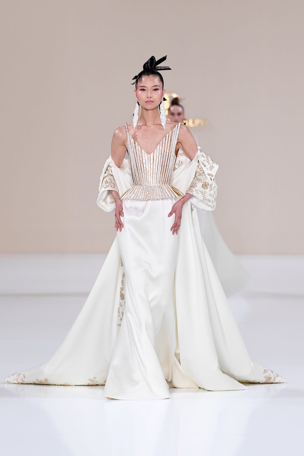 Model wearing an ornate white gown on the runway.