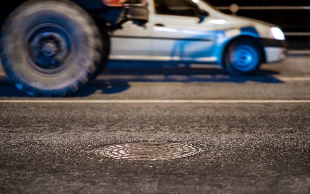 Sewer manhole on asphalt at night, cars passing by