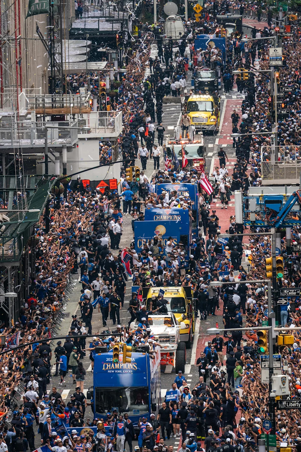 Crowds lining the street celebrate a championship parade with vehicles carrying athletes and team personnel