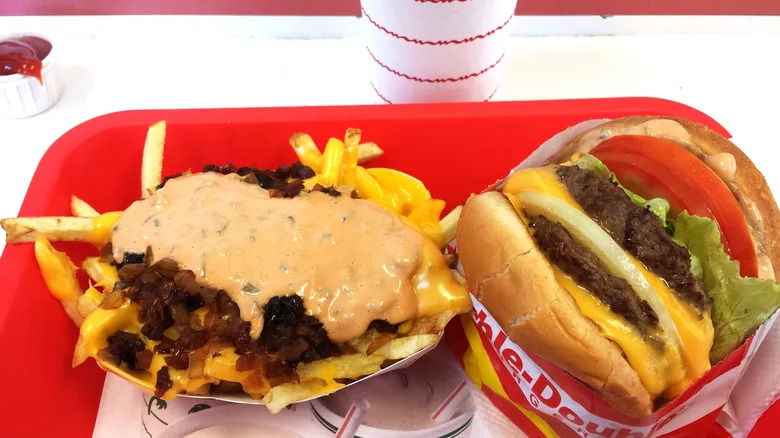 Animal-style fries, consisting of grilled onions, cheese, and spread, sit next to a double-double burger in a classic red tray.