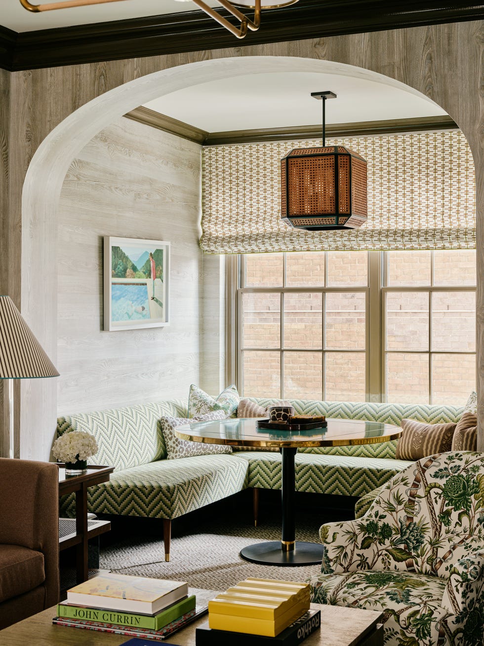 Cozy nook with green zigzag-patterned seating, striped armchair, and round table under a wooden pendant light.