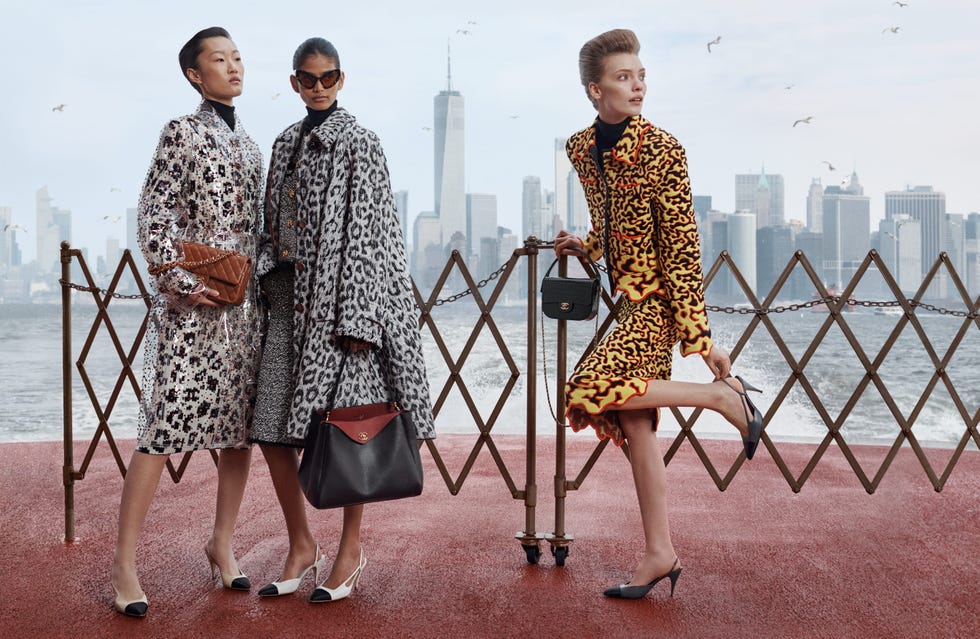 Models in patterned coats pose on a red walkway with a city skyline in the background.