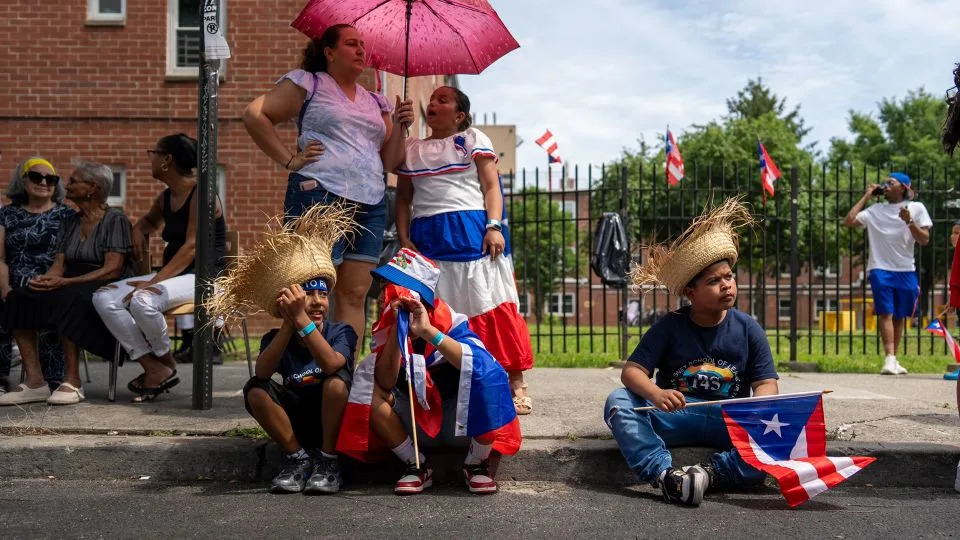 A family shares an umbrella to beat the New York heat while two boys wear traditional pava straw hats. - David Dee Delgado for CNN