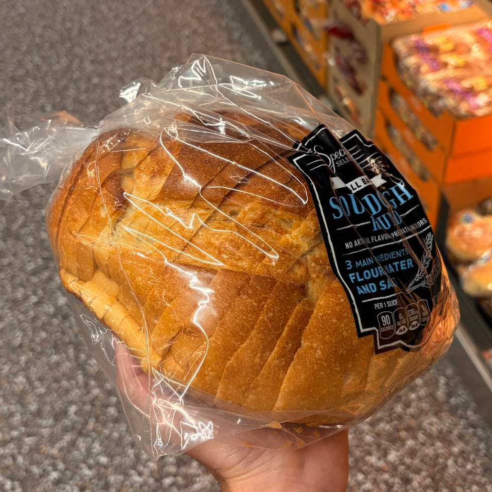 Person holding packaged loaf of sourdough bread in grocery store aisle.