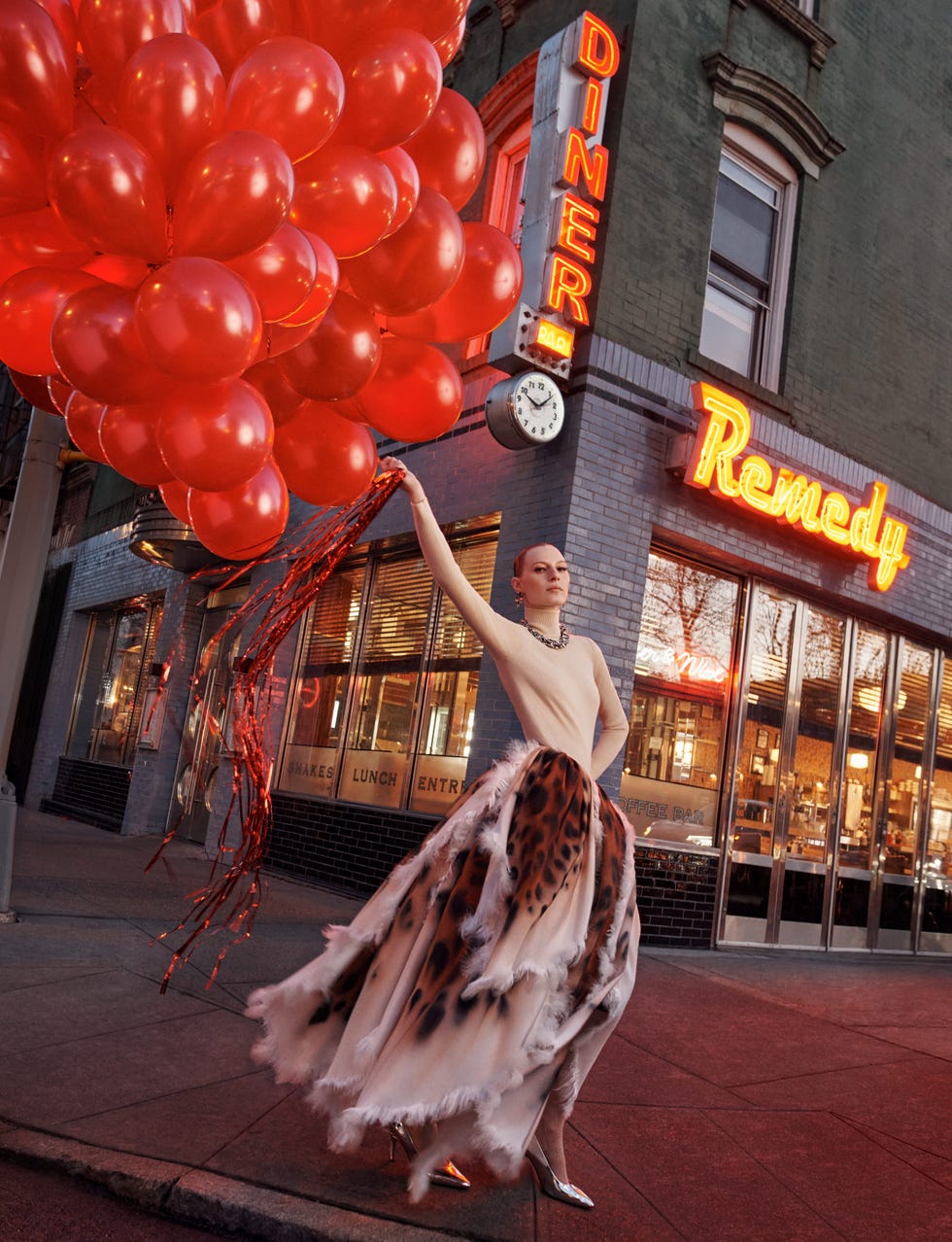 Fashionable person with red balloons in front of a retro diner with vibrant neon signs.